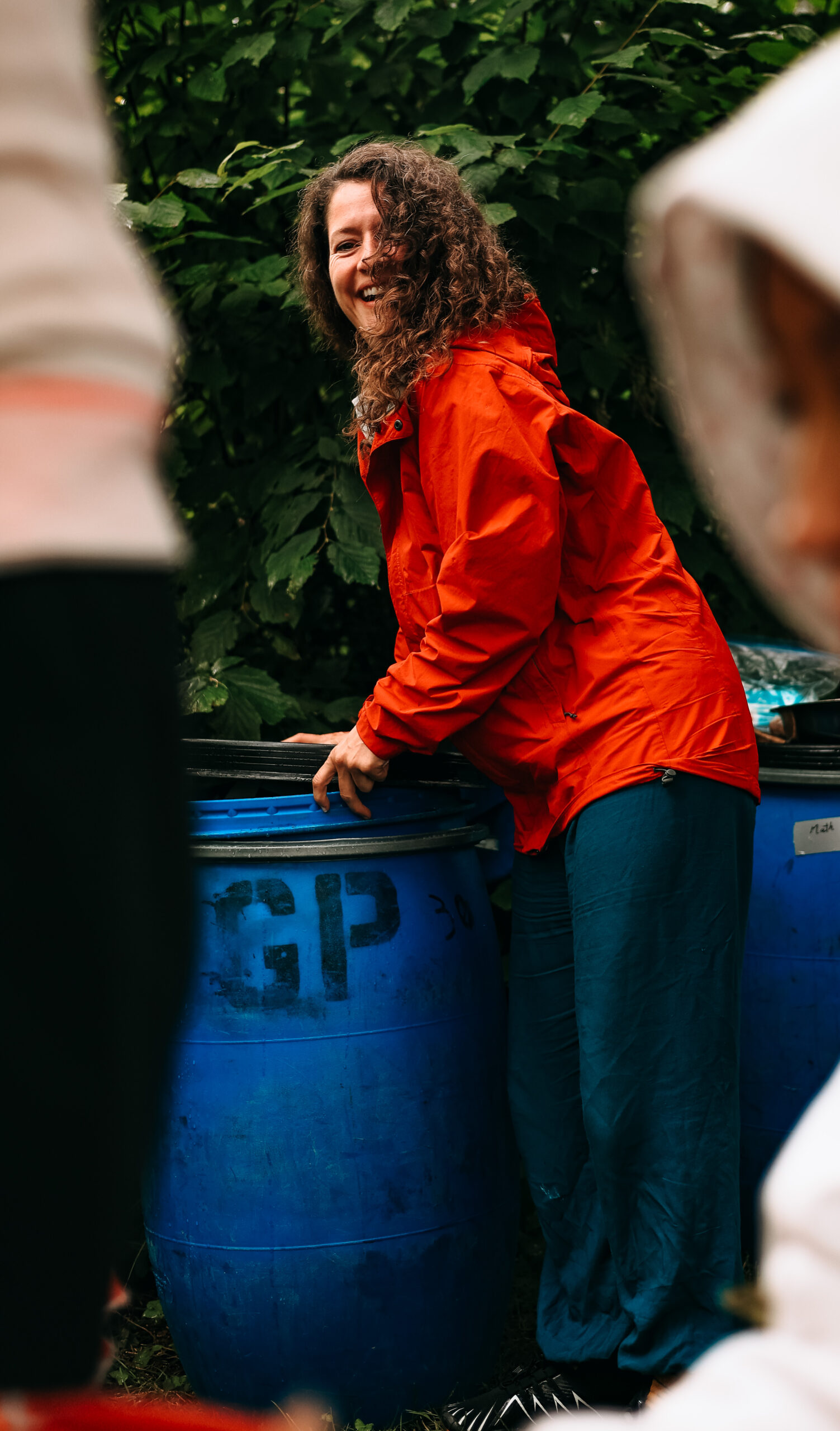 Femme avec manteau orange vif qui tient un baril bleu avec écriture GP