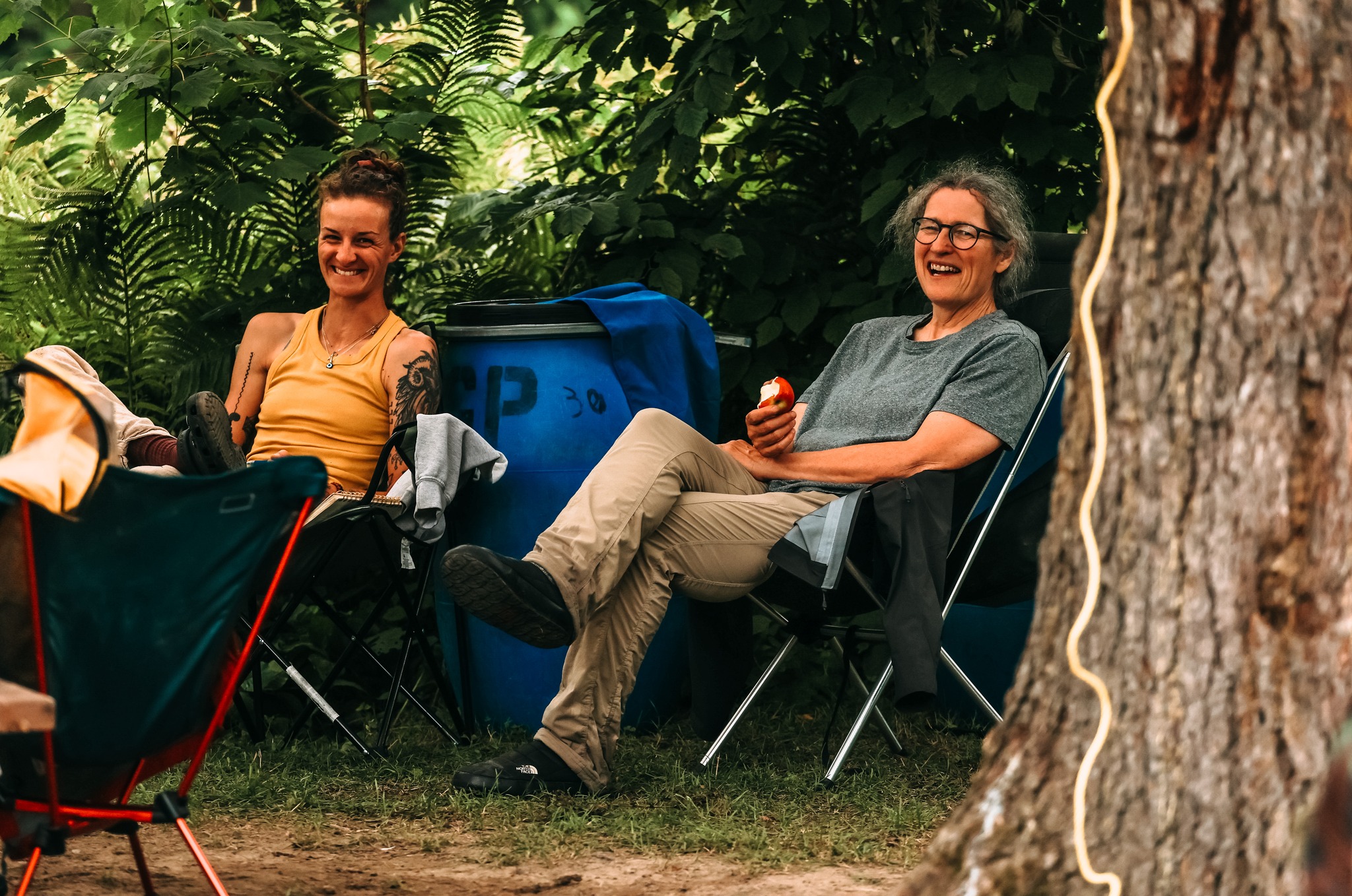 deux femmes souriantes dans des chaises de camping à l'extérieur, tasse à la main
