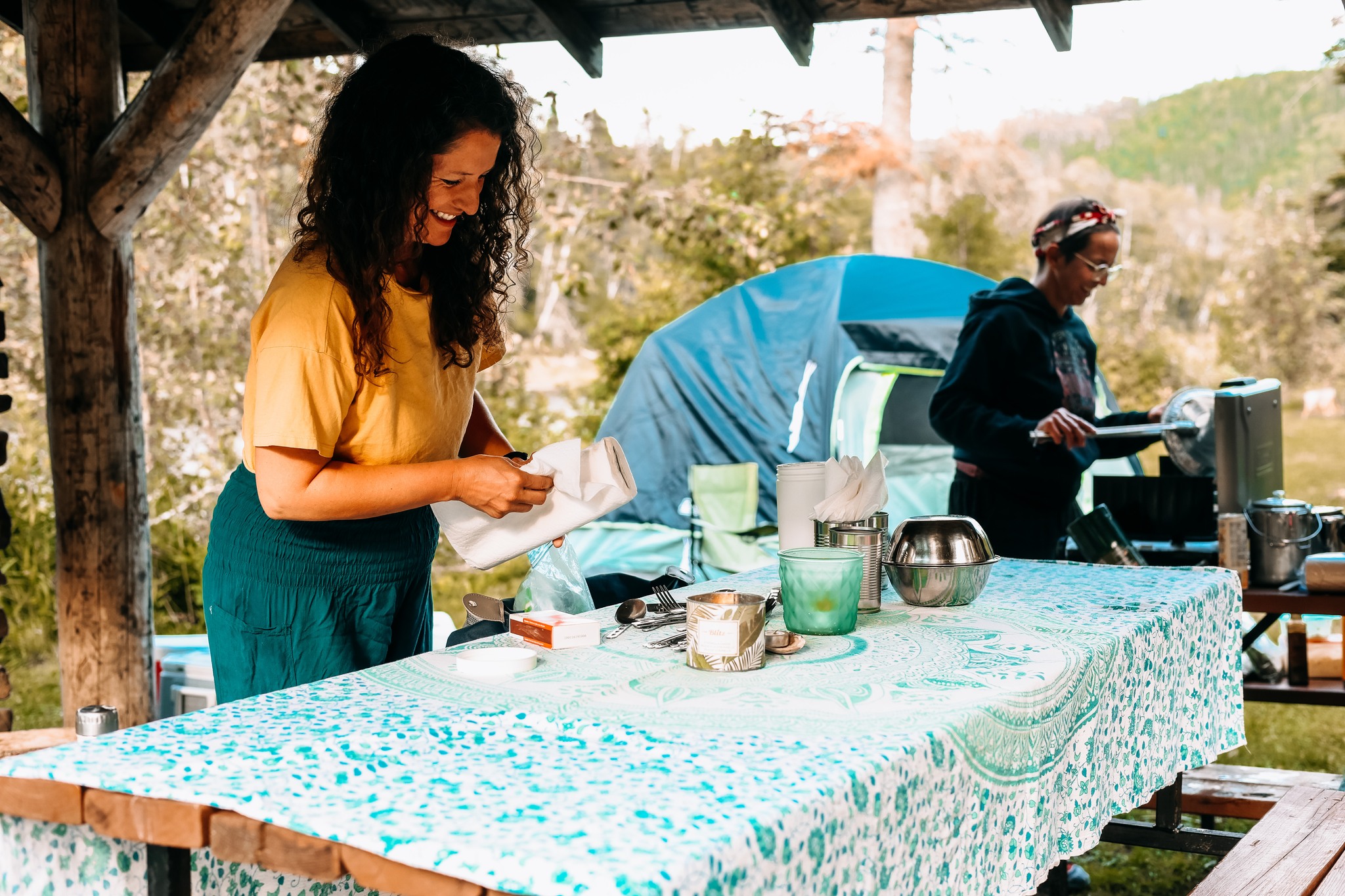 Femme au cheveux frisés et chandail jaune qui cuisine sur une table pic-nic à l'extérieur